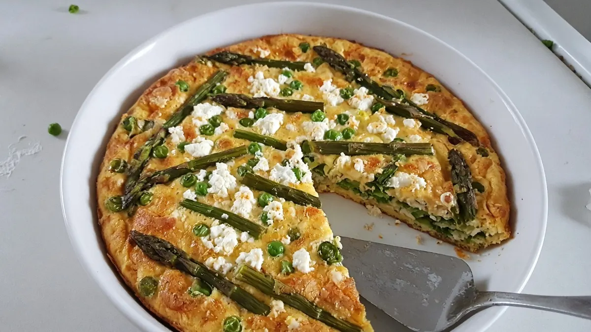 Asparagus, pea and feta frittata in a white baking dish with one slice cut out