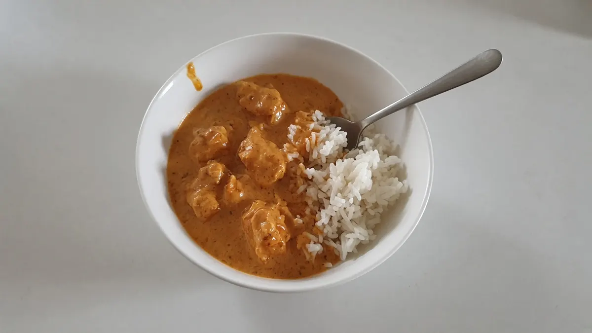 Butter chicken in a creamy orange tomato sauce with steamed white rice in a white bowl