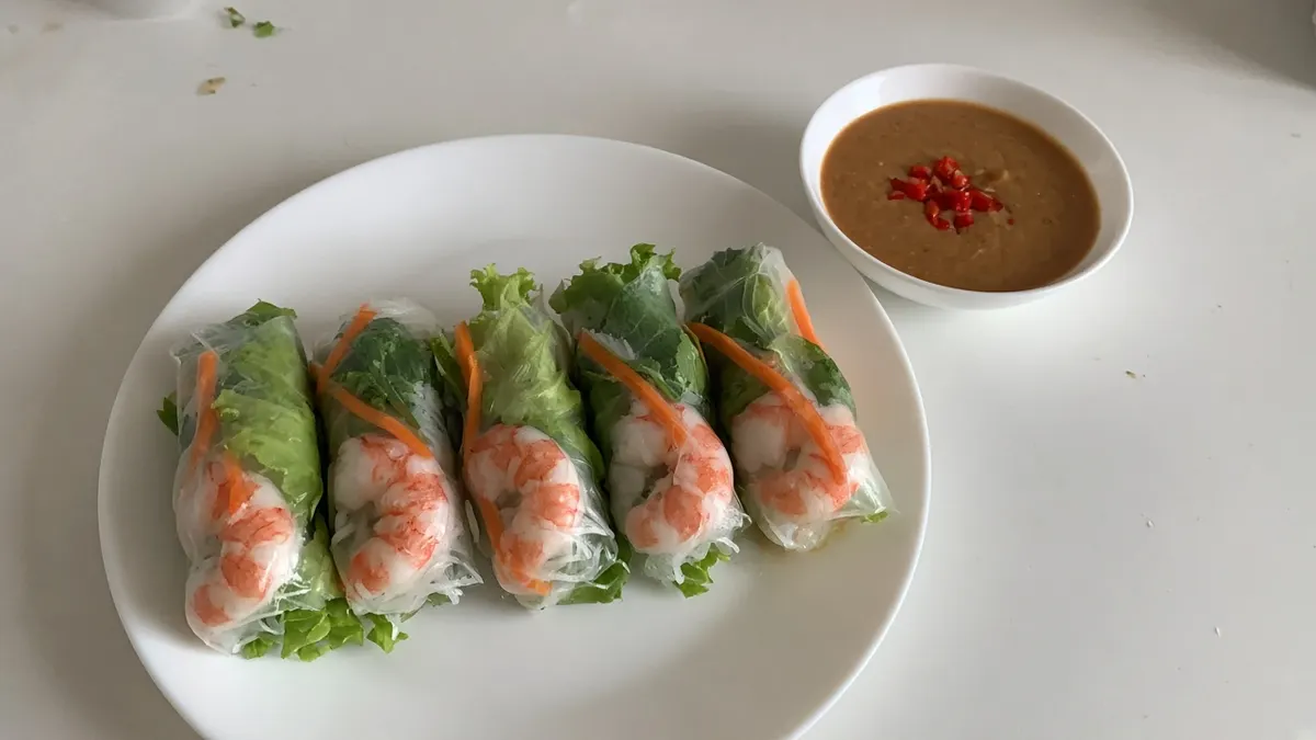 Five prawn rice paper rolls with lettuce and carrot and a bowl of peanut dipping sauce