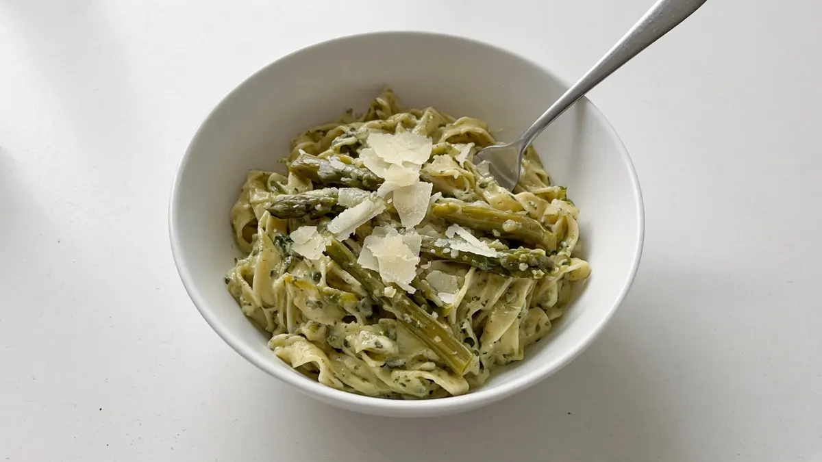 Bowl of tagliatelle in asparagus cream sauce with asparagus pieces and parmesan shavings and a fork