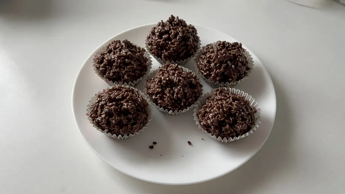 Six chocolate crackles in paper patty cases on a white plate