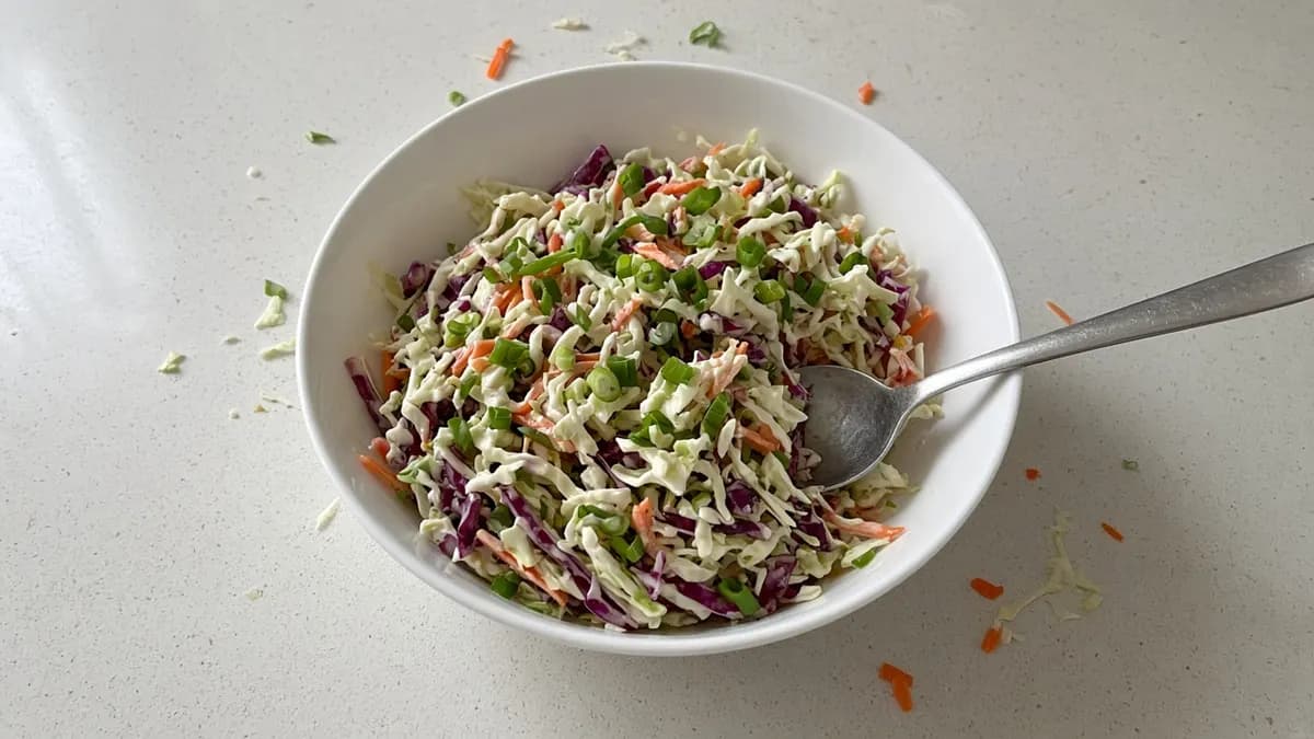 Bowl of creamy coleslaw with green and red cabbage, carrot and spring onion and a spoon