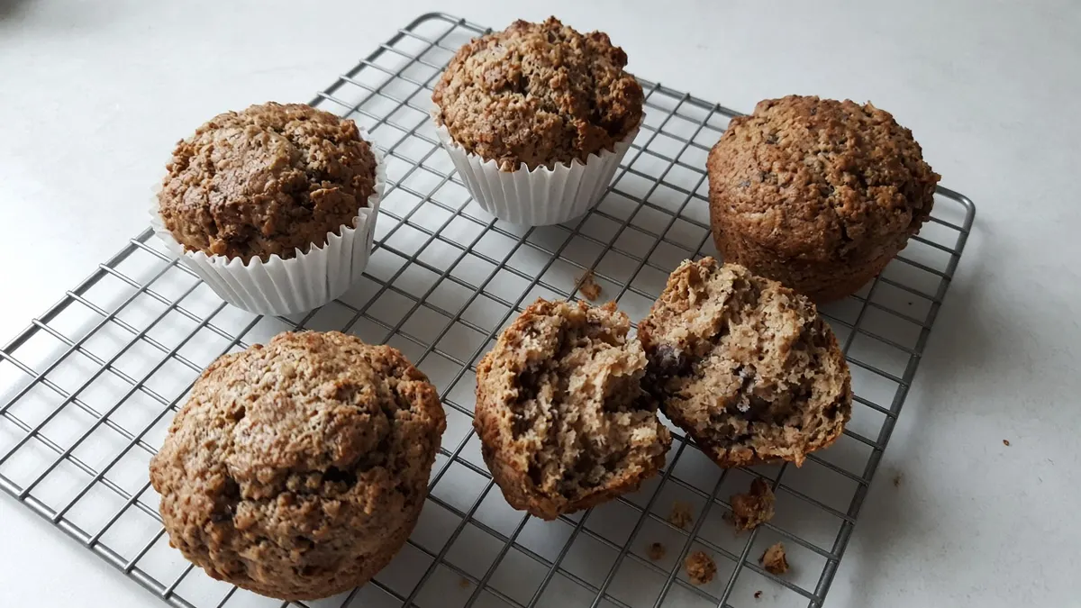 Whole-wheat banana muffins cooling on a wire rack, one broken open to show the crumb