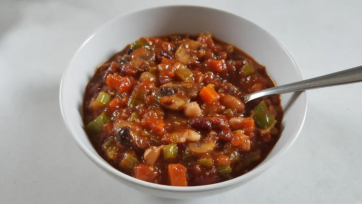 Vegetarian chili with kidney beans, carrots, peppers and corn in a white bowl with a spoon