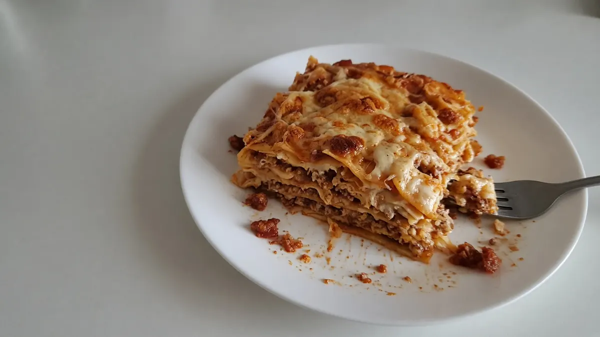 A slice of keto lasagna with melted cheese and meat sauce on a white plate with a fork
