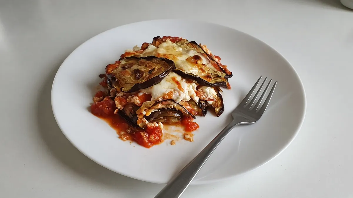 Eggplant lasagna layered with tomato sauce and melted cheese on a white plate with a fork
