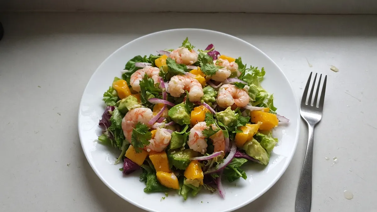 Salad of peeled prawns, diced mango, avocado, red onion and coriander on a white plate