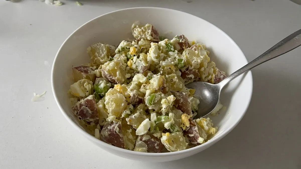Bowl of potato salad with chopped boiled egg and spring onion in a creamy dressing