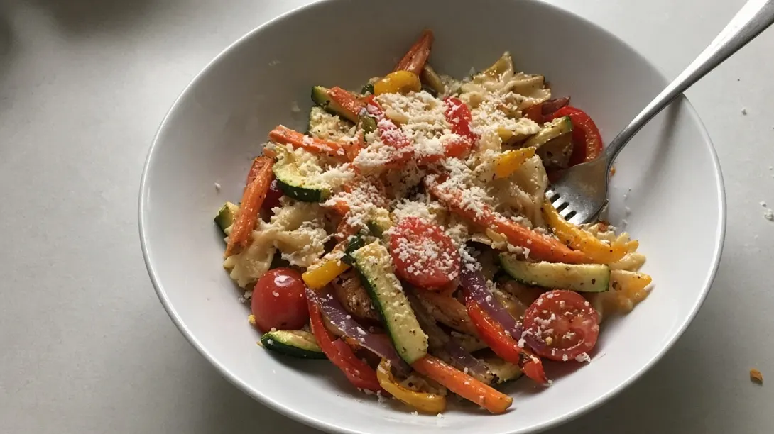 Farfalle pasta primavera with roasted carrot, zucchini and capsicum strips, cherry tomatoes and parmesan in a white bowl