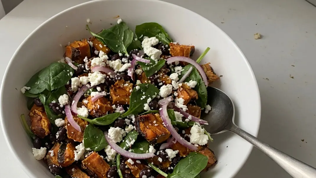 Roasted sweet potato salad with black beans, baby spinach, feta and red onion in a white bowl