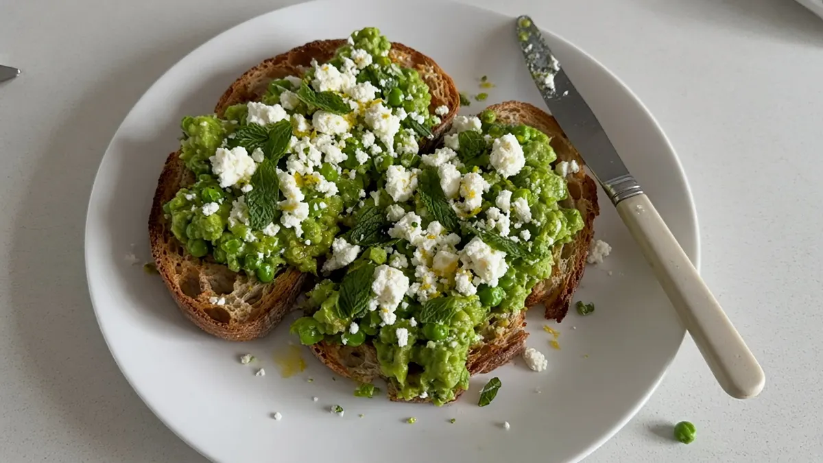 Toasted sourdough topped with smashed peas, crumbled feta and mint on a white plate