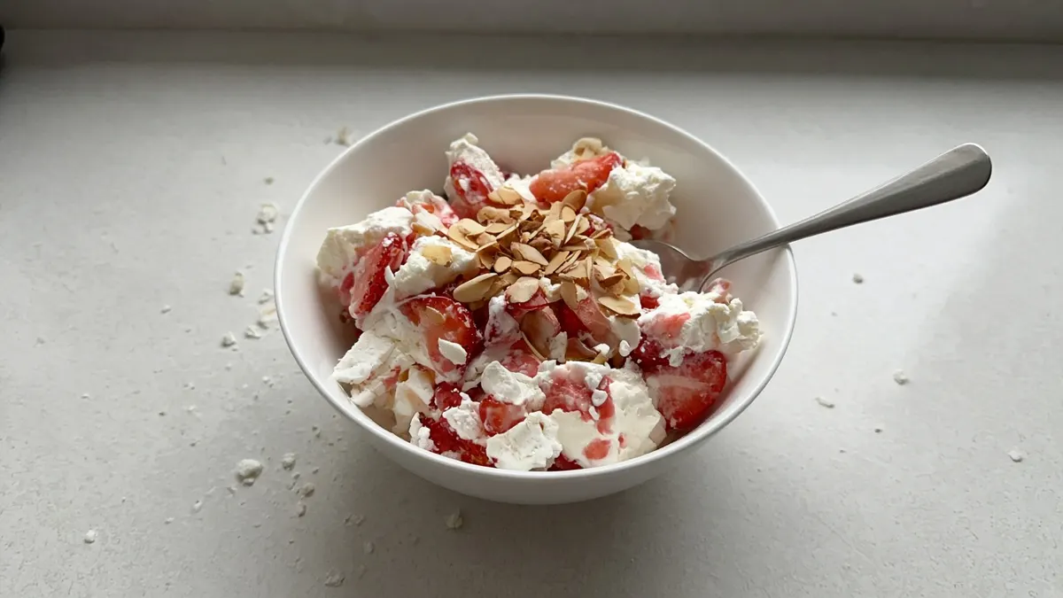 Bowl of Eton mess with whipped cream, broken meringue, strawberries and flaked almonds
