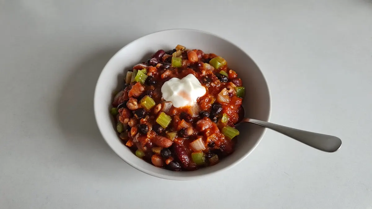 Three-bean vegetarian chili topped with a spoonful of sour cream in a white bowl with a spoon