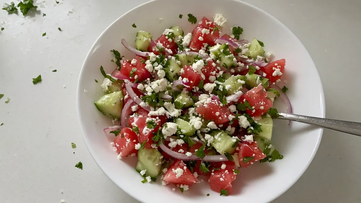Watermelon, cucumber and feta salad with red onion and coriander in a white bowl